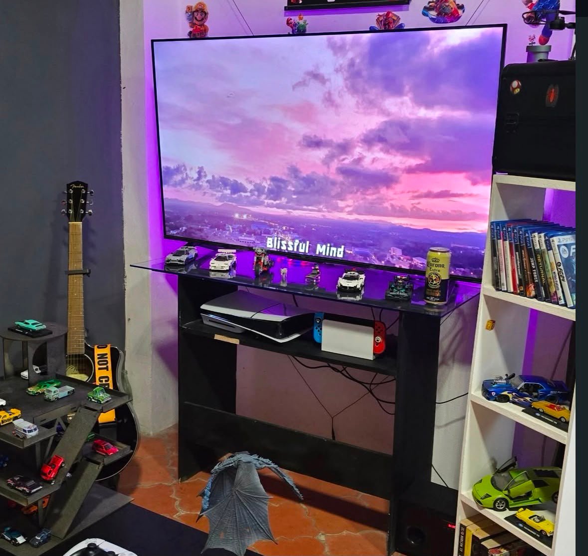 Zona lounge con PlayStation, Nintendo Switch, colección de autos a escala y guitarra